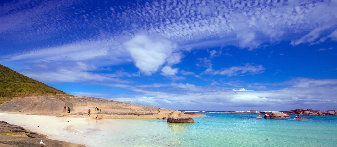 A sandy cove with clear turquoise water beside smooth sloping granite under a bright blue sky, on Western Australia's south coast